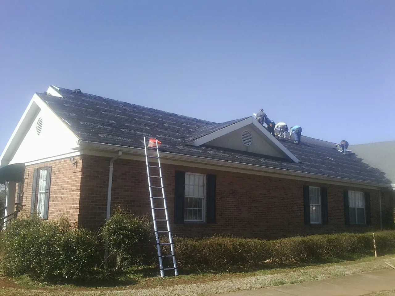 Crew tearing shingles off a brick ranch roof with a ladder set — Emergency Roof Repair work by our crew in Garvin