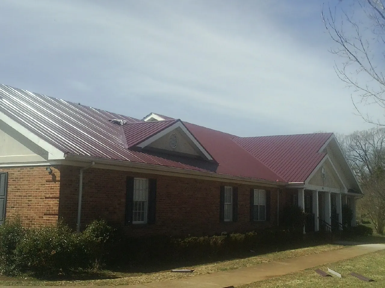 Red metal roof with gabled entries on a long brick building, from a Hail Damage Roof Repair job in Garvin