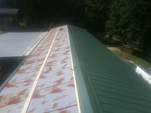 Old rusted panels beside newly installed green metal roofing — Wind Damage Roof Repair by Roofing Brothers in Garvin