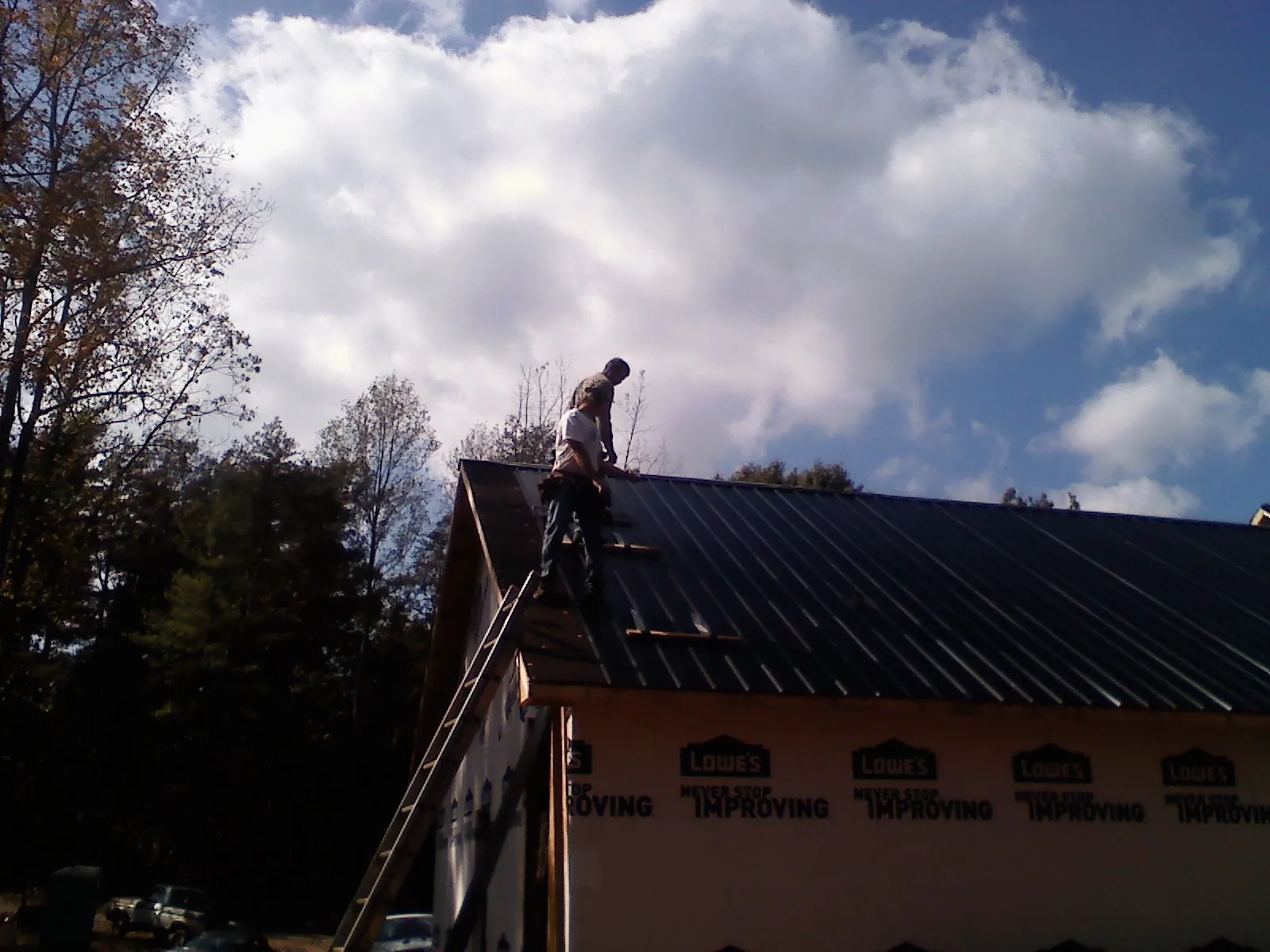 Roofer fastening dark metal panels high against a cloudy sky, from a Roof Inspection job in Garvin