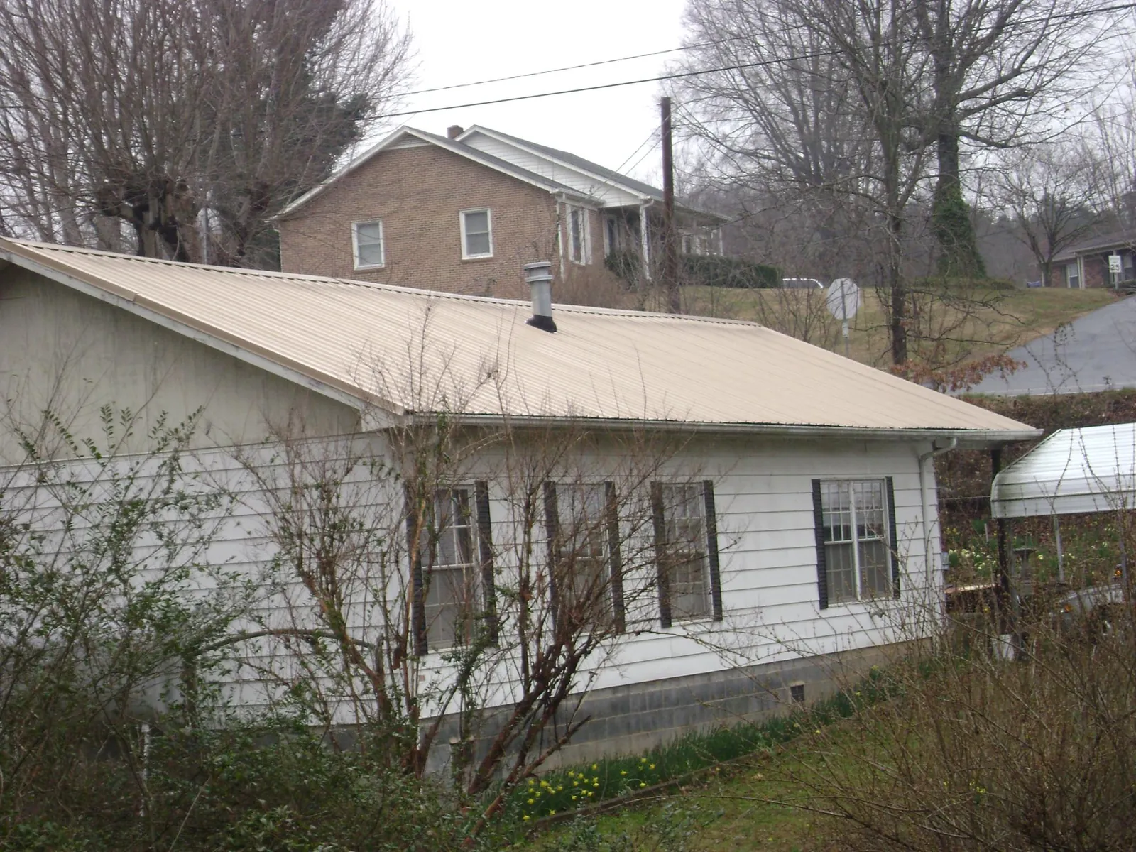 Tan metal roof on a white sided house set into a hillside — Commercial Roofing by Roofing Brothers in Garvin