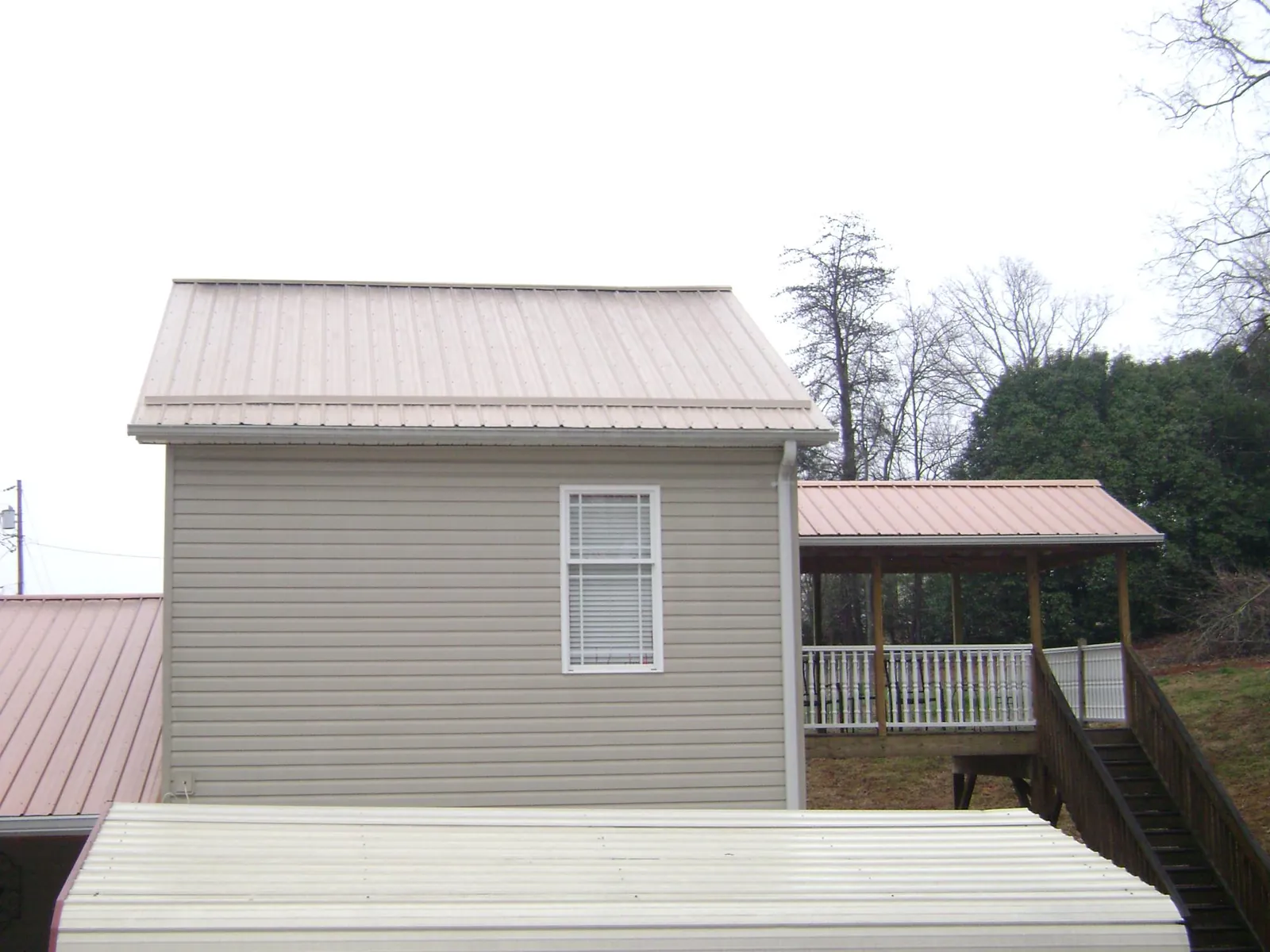 Tan metal roofs on a two story addition and attached porch, from a Roof Replacement job in Garvin