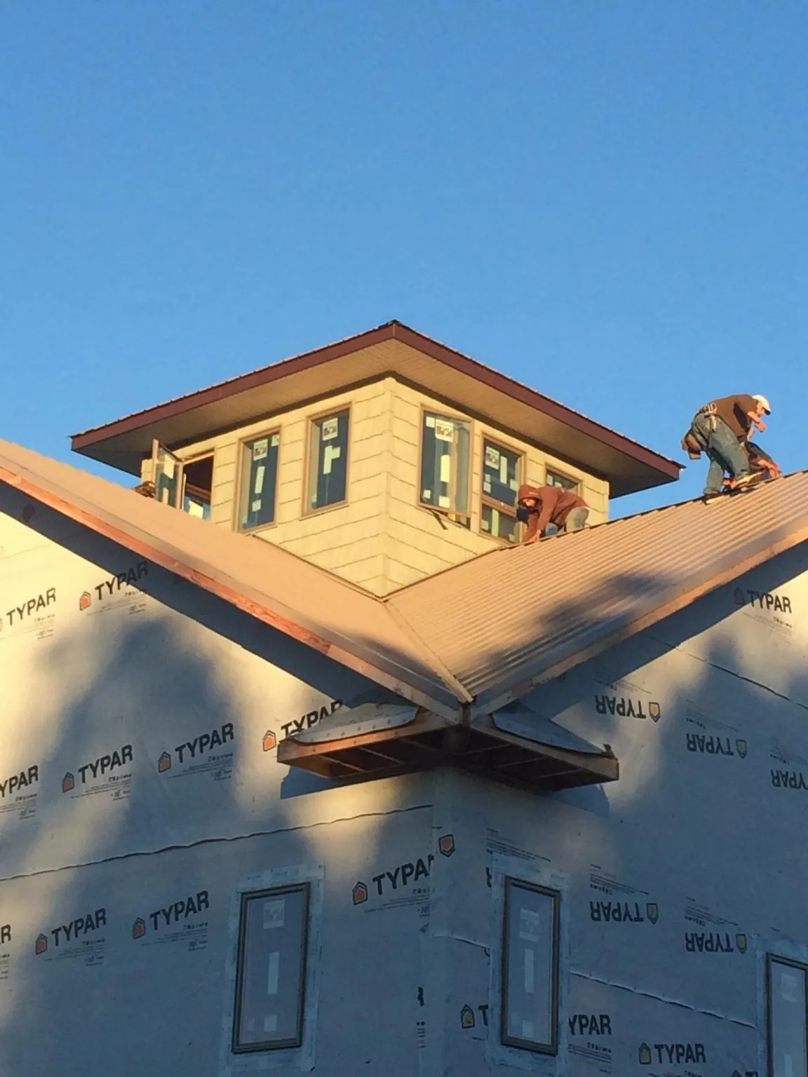 Roofers working around a rooftop cupola on a new metal roof at sunset — Roof Waterproofing in Garvin by Roofing Brothers